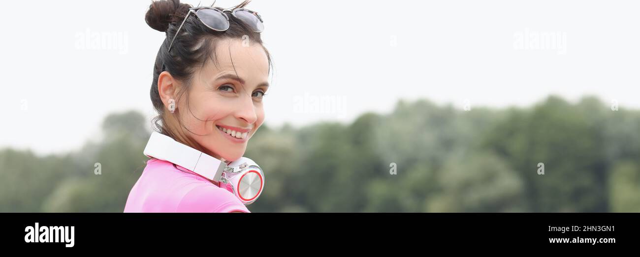 Giovane donna sorridente con le cuffie sul collo in piedi sul ponte Foto Stock
