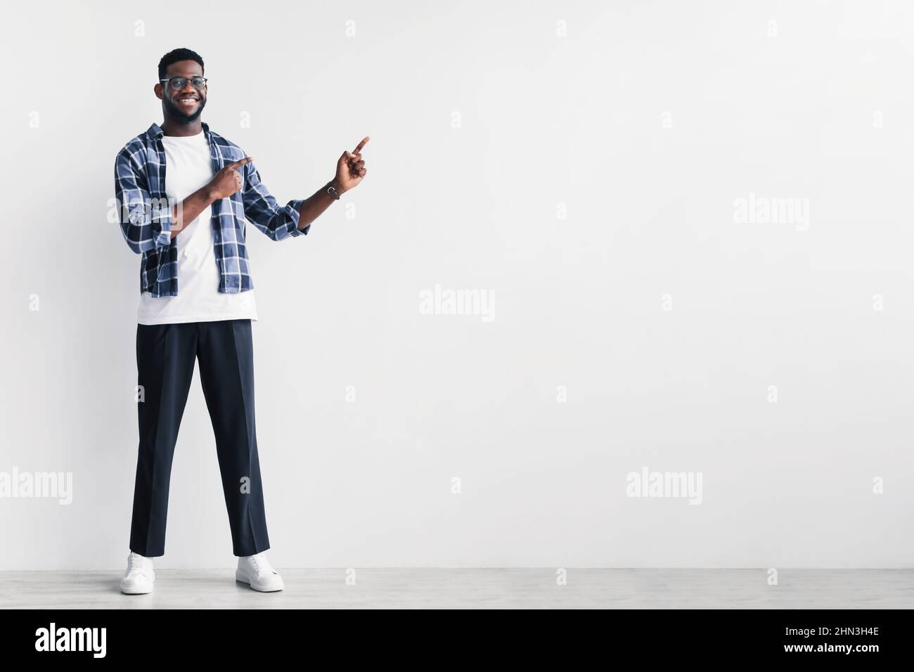 Bel giovane uomo nero che punta da parte a spazio copia per la tua pubblicità contro la parete bianca studio Foto Stock