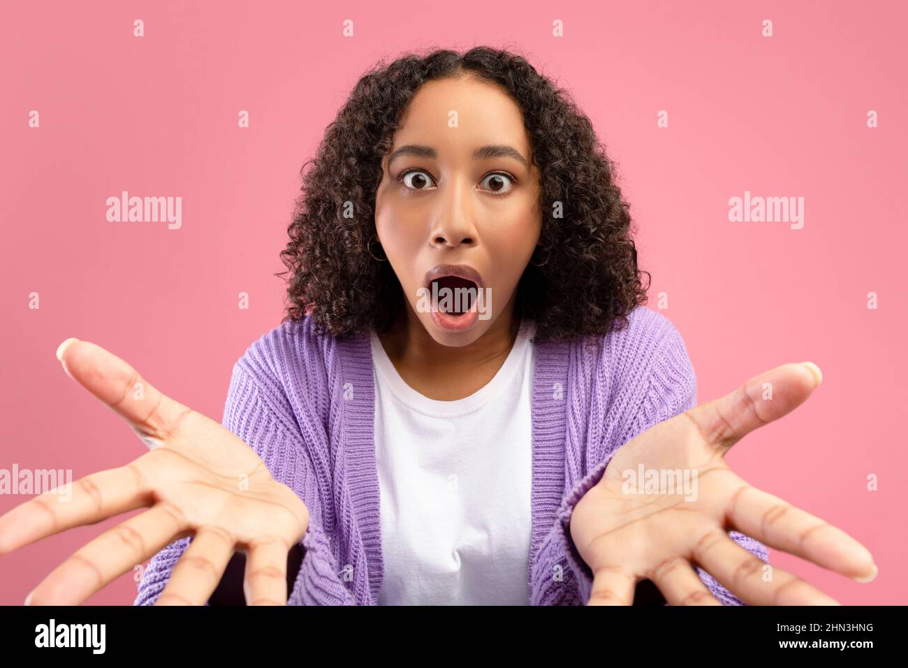 Donna nera scioccata che guarda la fotocamera a bocca aperta, esprimendo stupore su sfondo rosa studio Foto Stock