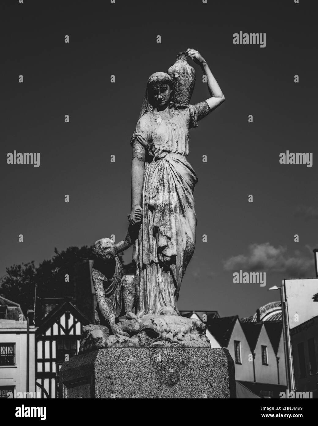 Scala di grigi scatto verticale di una bella statua donna che tiene una caraffa e la mano del bambino Foto Stock