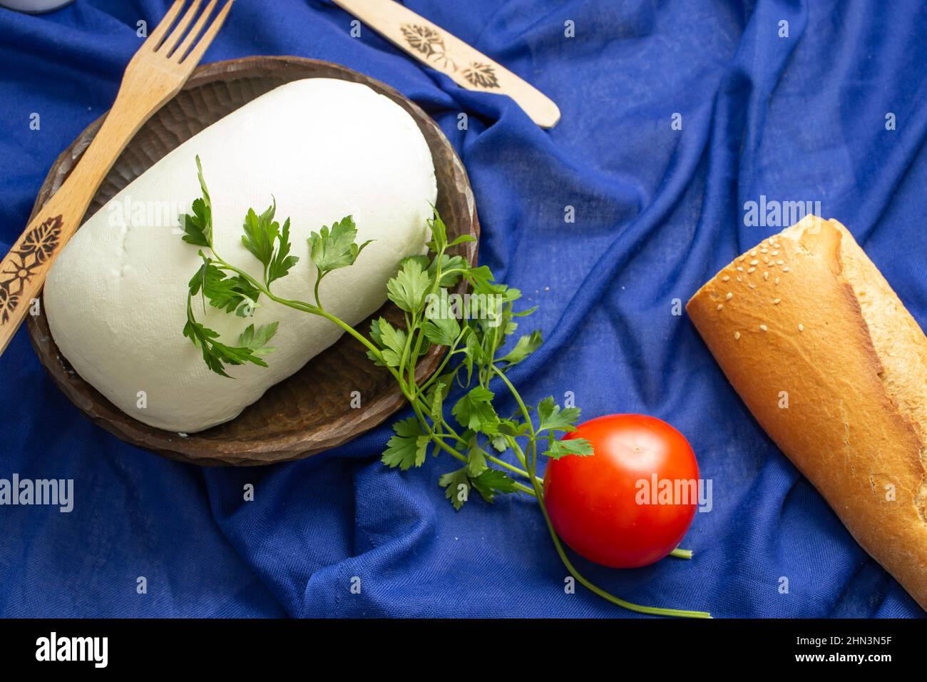Formaggio contadino su una ciotola di legno con pane su sfondo tessile blu Foto Stock