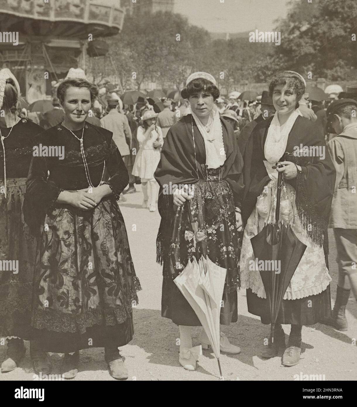 Foto d'epoca di ragazze francesi in abito tradizionale con berretti in pizzo e grembiuli di seta in fiera. 1900s Foto Stock