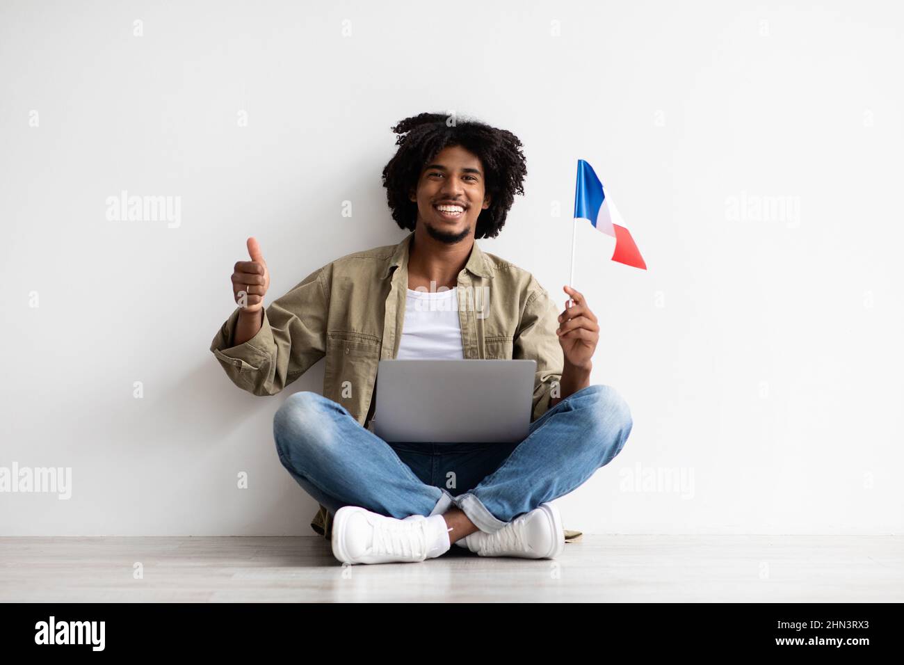 Impara le lingue online. Ritratto di Black Guy con laptop e bandiera francese Foto Stock