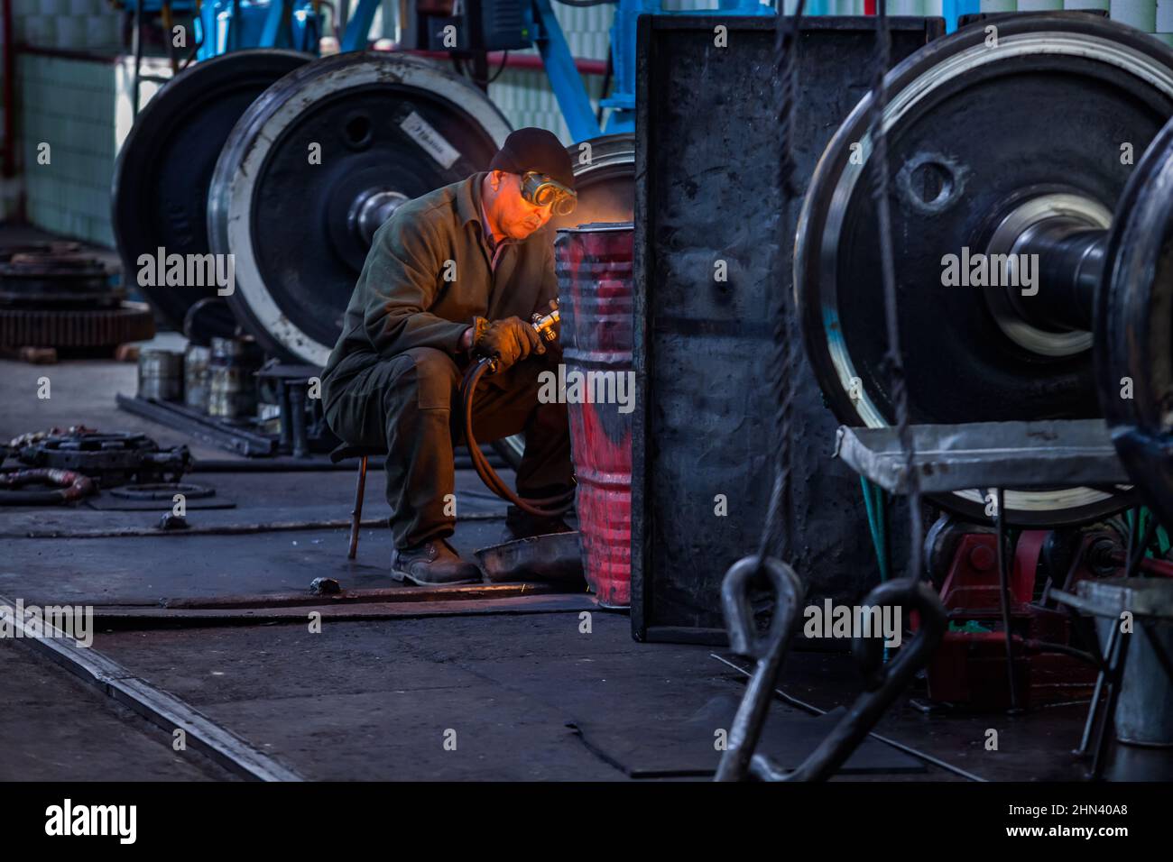 Kazaly, Kazakistan - 02 maggio 2012: Impianto di riparazione locomotiva. Senior Asian Welder lavora tra i treni ruote. Foto Stock