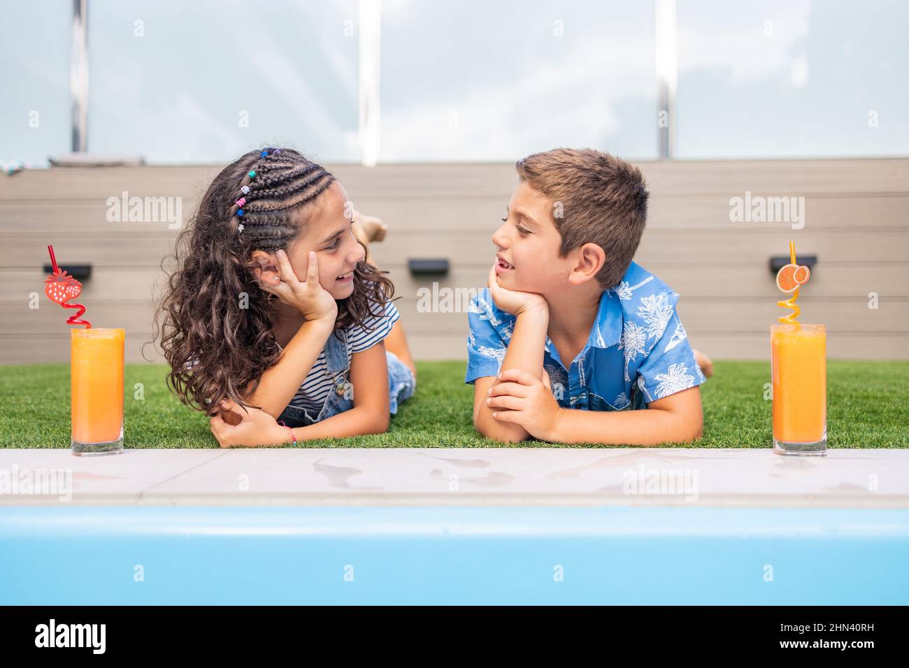 Ritratto di due bambini che bevono succo d'arancia in piscina Foto Stock