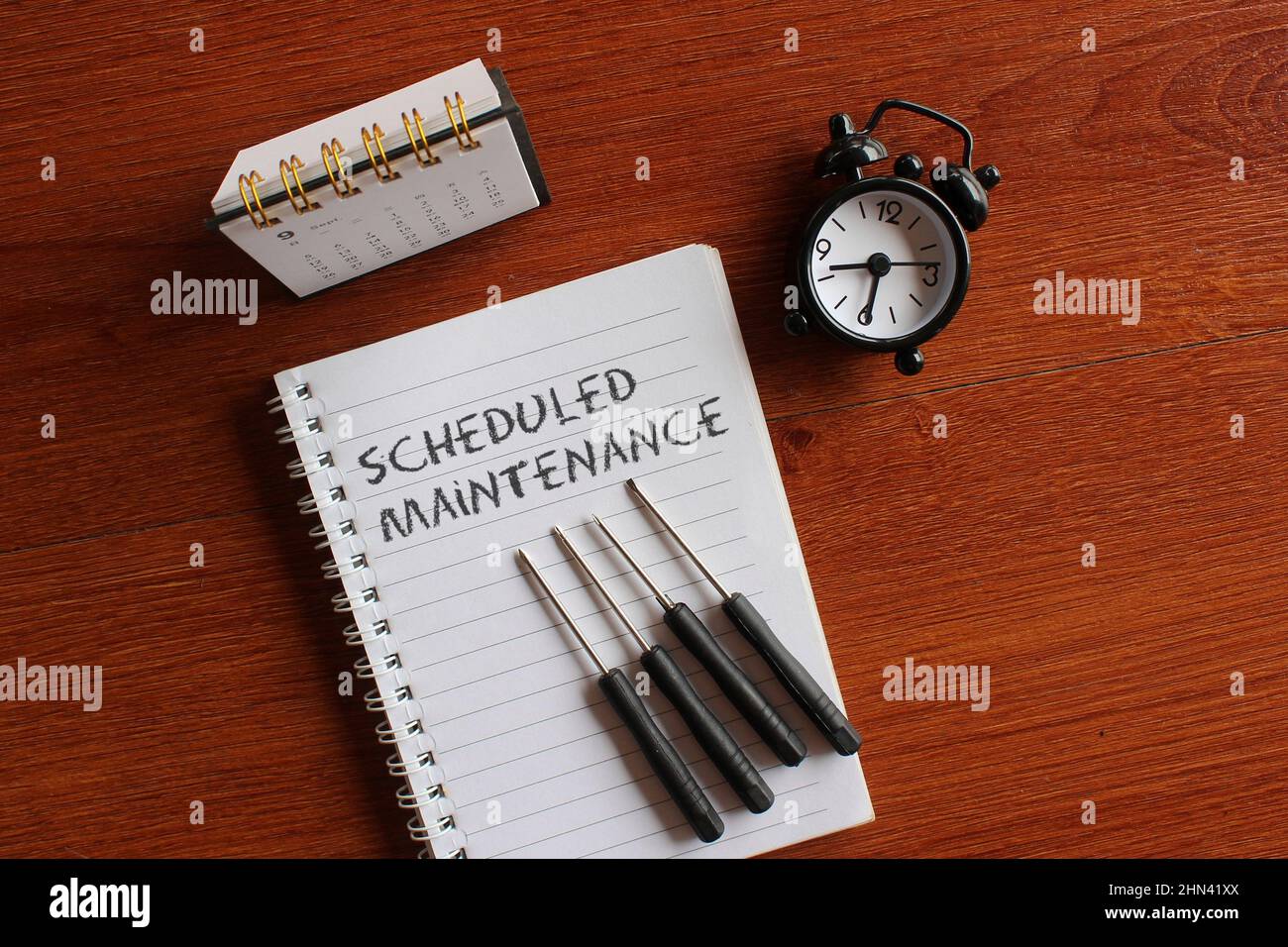 Immagine dall'alto di calendario, sveglia, cacciavite e libro con testo MANUTENZIONE PROGRAMMATA. Foto Stock