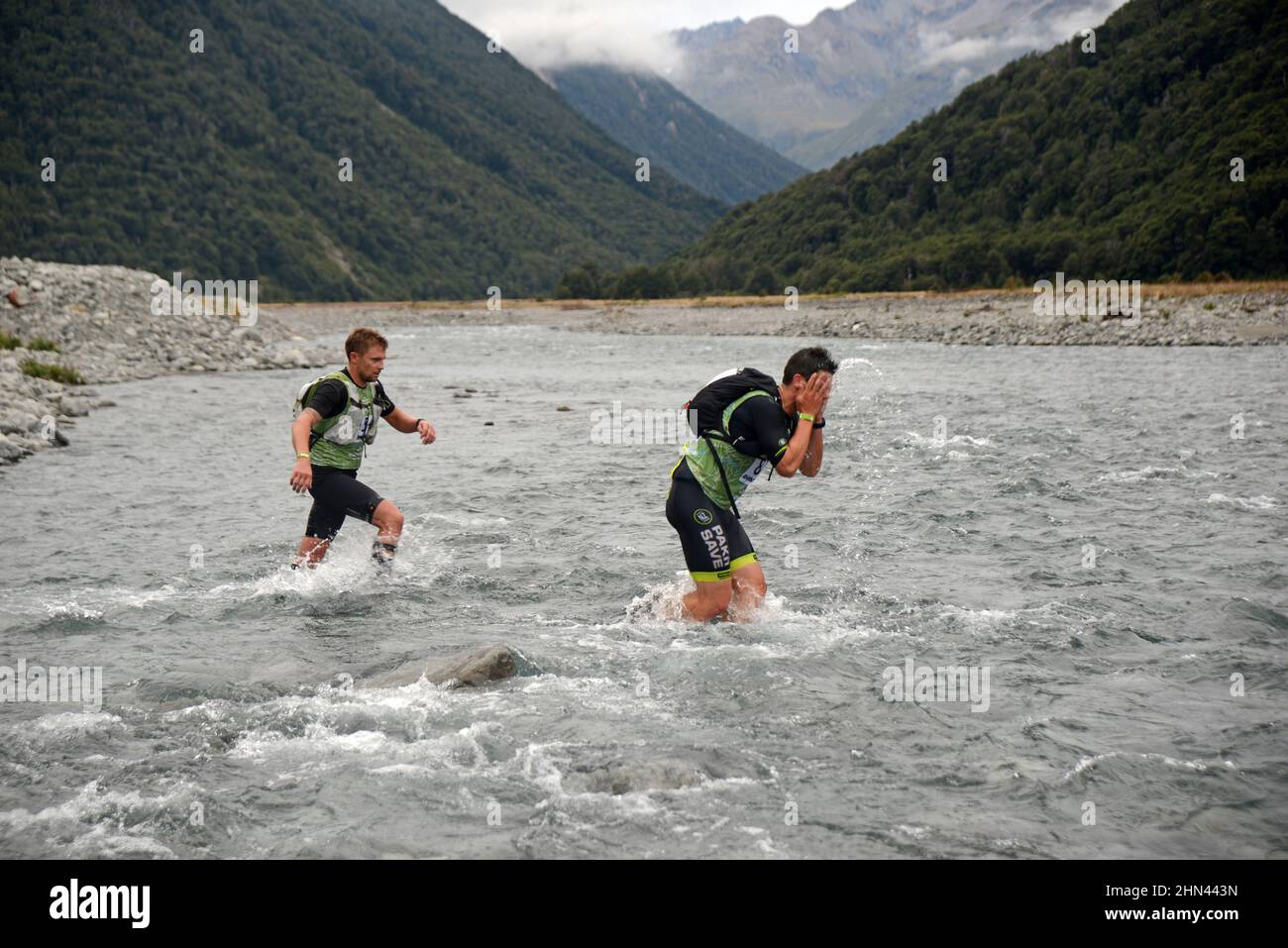 ARTHURS PASS, NUOVA ZELANDA, 12 FEBBRAIO 2022; il concorrente 87 lava il volto nel fiume Bealey mentre corre contro il concorrente 54 nel triathlon Coast to Coast Foto Stock