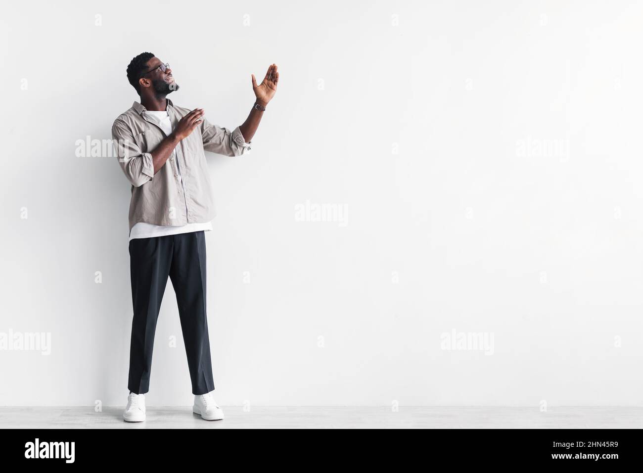 Tutta la lunghezza del giovane uomo nero bello che punta allo spazio vuoto per il vostro disegno dell'annuncio contro la parete bianca dello studio Foto Stock