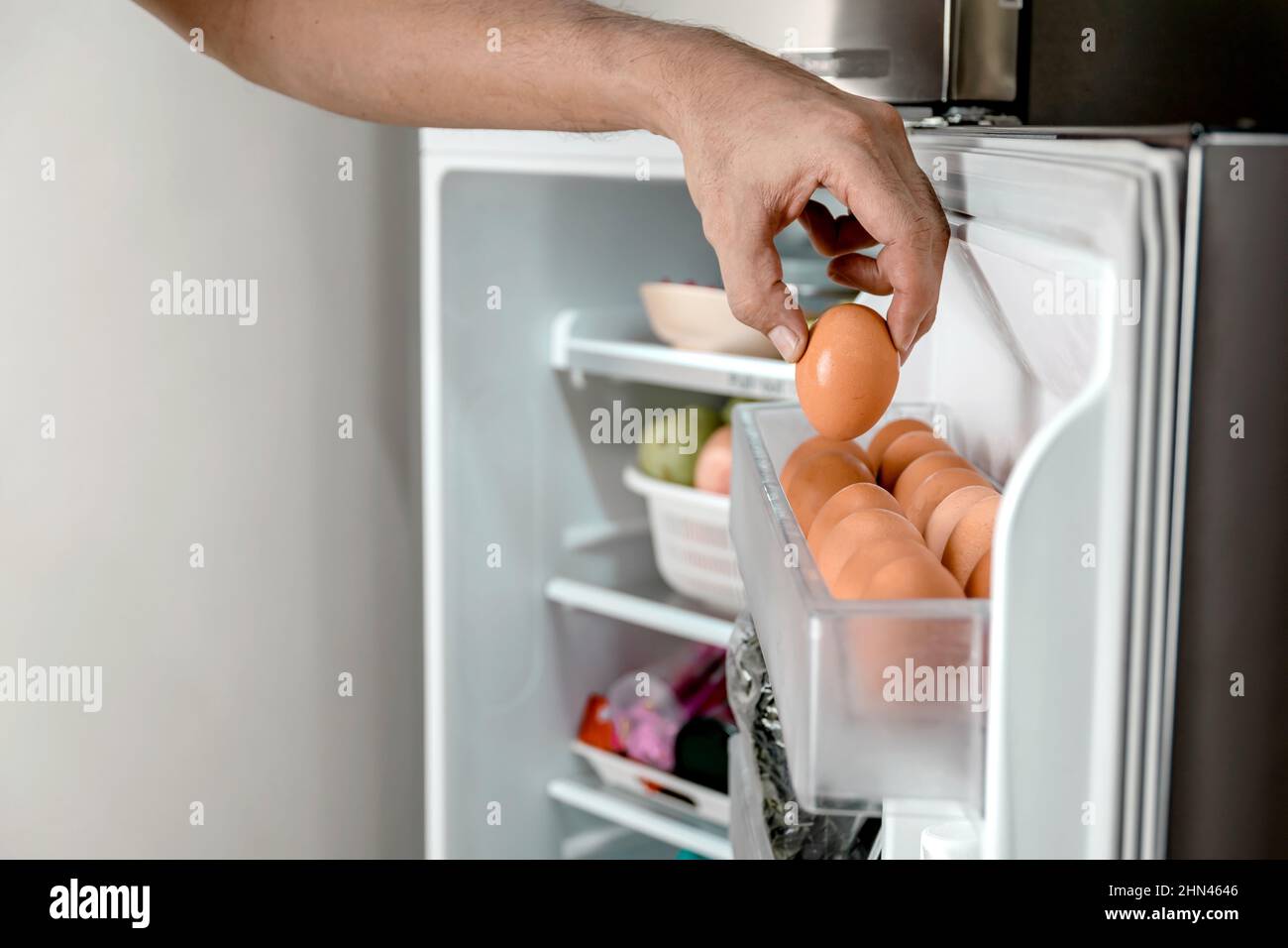 Primo piano mani umane mettere le uova di pollo nel vano per la deposizione delle uova nel frigorifero. Foto Stock
