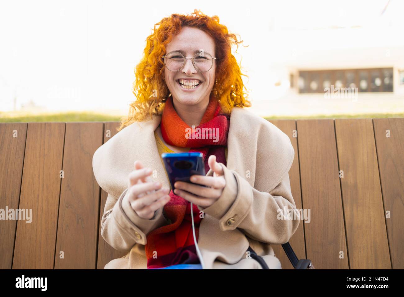 Giovane donna sorridente mentre usa il suo smartphone su una panca Foto Stock