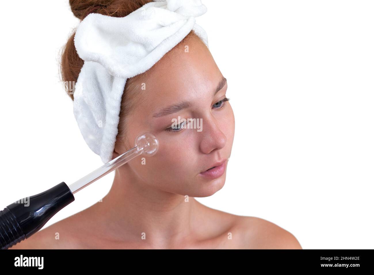 Ritratto isolato di giovane donna caucasica senza make up con fascia sulla testa che tiene darsonval sul viso guardando giù su sfondo bianco Foto Stock