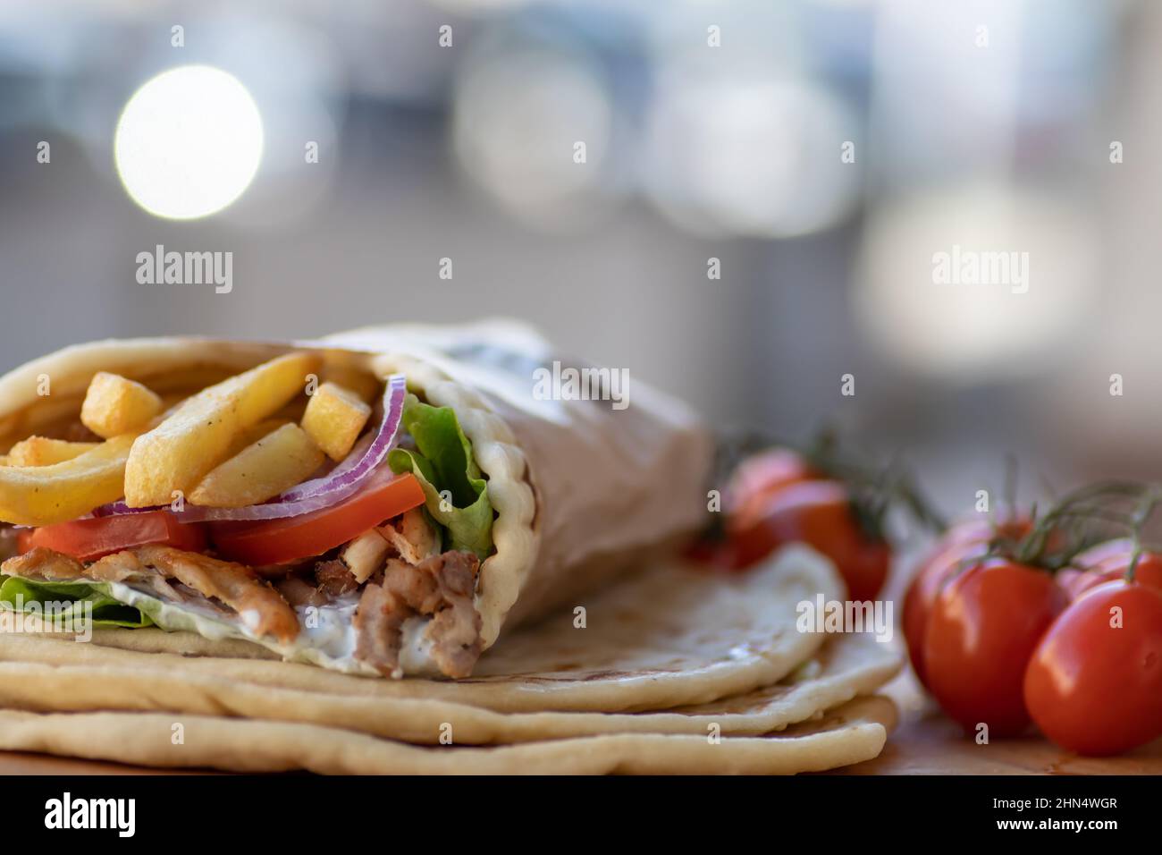 Cibo di strada greco Gyros da portare via, ben avvolto con pomodoro, souvlaki, insalata greca, cipolla e patatine fritte Foto Stock