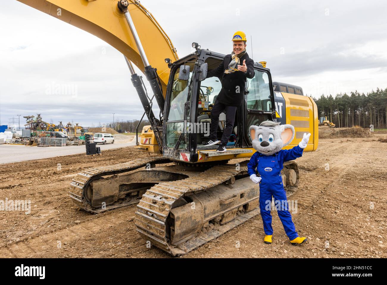 Ruggine, Germania. 14th Feb 2022. Il trombettista, cantante e presentatore Stefan Mross si esibisce presso il cantiere della nuova arena per 'Immer wieder Sonntags' su un digger davanti alla mascotte di Europa-Park 'Euro-Maus'. Europa-Park ha demolito la vecchia arena della mostra 'Immer wieder Sonntags' per la costruzione di una nuova montagne russe e sta costruendo una nuova e più grande arena altrove. La prima trasmissione dello spettacolo nella nuova arena è prevista per il 12 giugno 2022. Credit: Rin/dpa/Alamy Live News Foto Stock