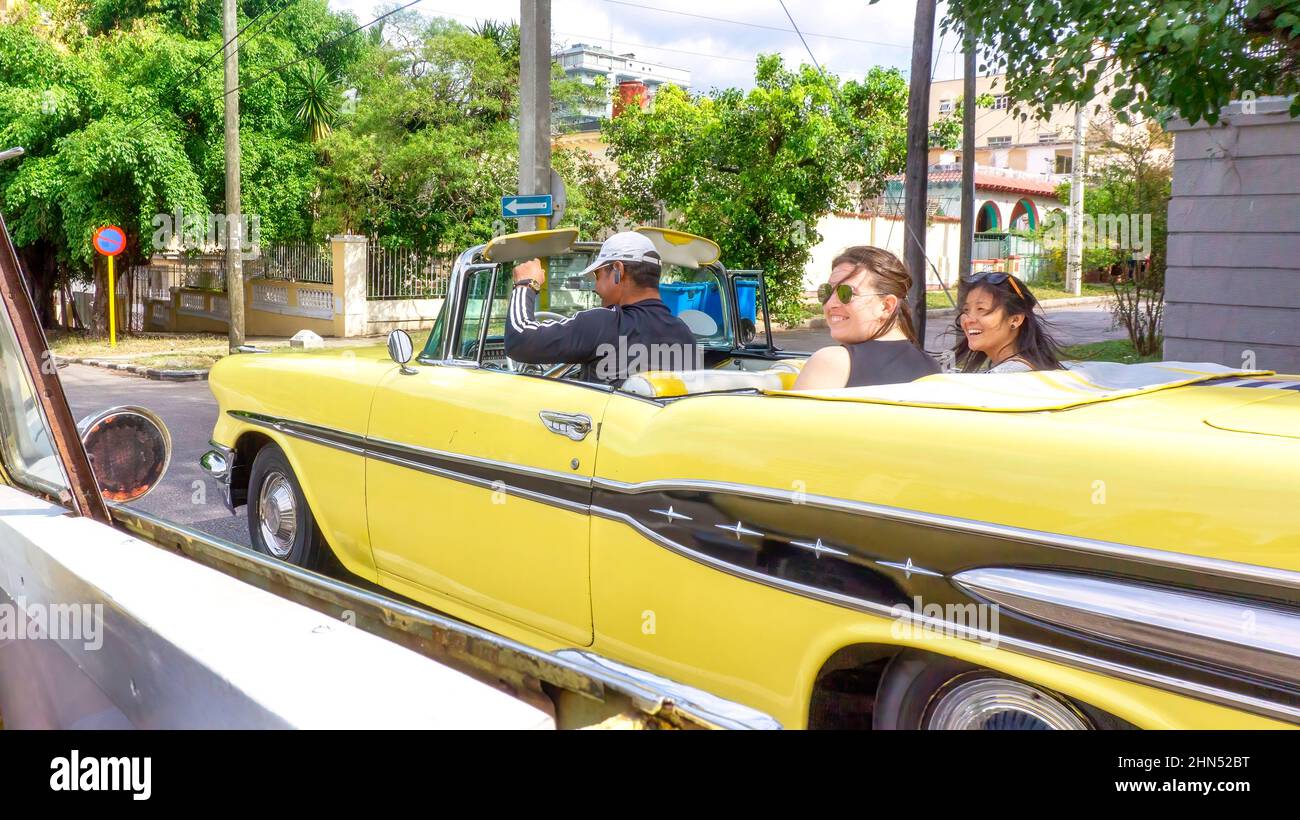 Due turisti stranieri che partecipano a un tour della città in un'auto convertibile d'epoca. Punto di vista di un altro turista nello stesso percorso. Foto Stock