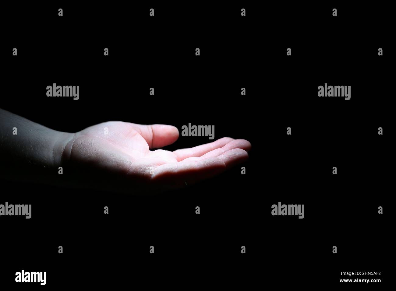 Il palmo di un uomo è illuminato da luce bianca al buio. Un gesto della mano. Isolare. Mano maschio. Foto Stock