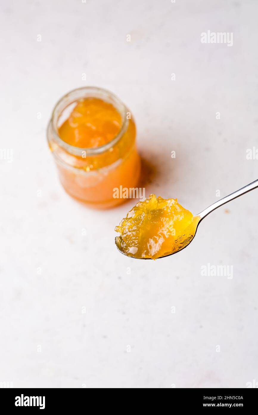 cucchiaio di marmellata di frutta con una bottiglia sullo sfondo, primo piano su una superficie bianca testurizzata con spazio copia, preso dall'alto Foto Stock