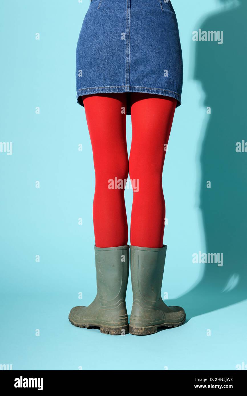 Vista posteriore della gonna in denim femminile non riconoscibile con collant rosso brillante e stivali verdi in piedi in studio Foto Stock