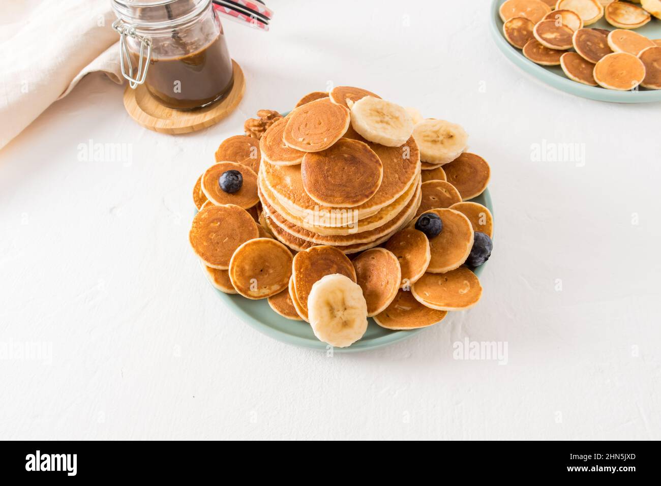 un assortimento di pancake su un piatto, pasta di cioccolato in un vaso su un tavolo bianco. deliziosa colazione per i bambini. sfondo bianco Foto Stock