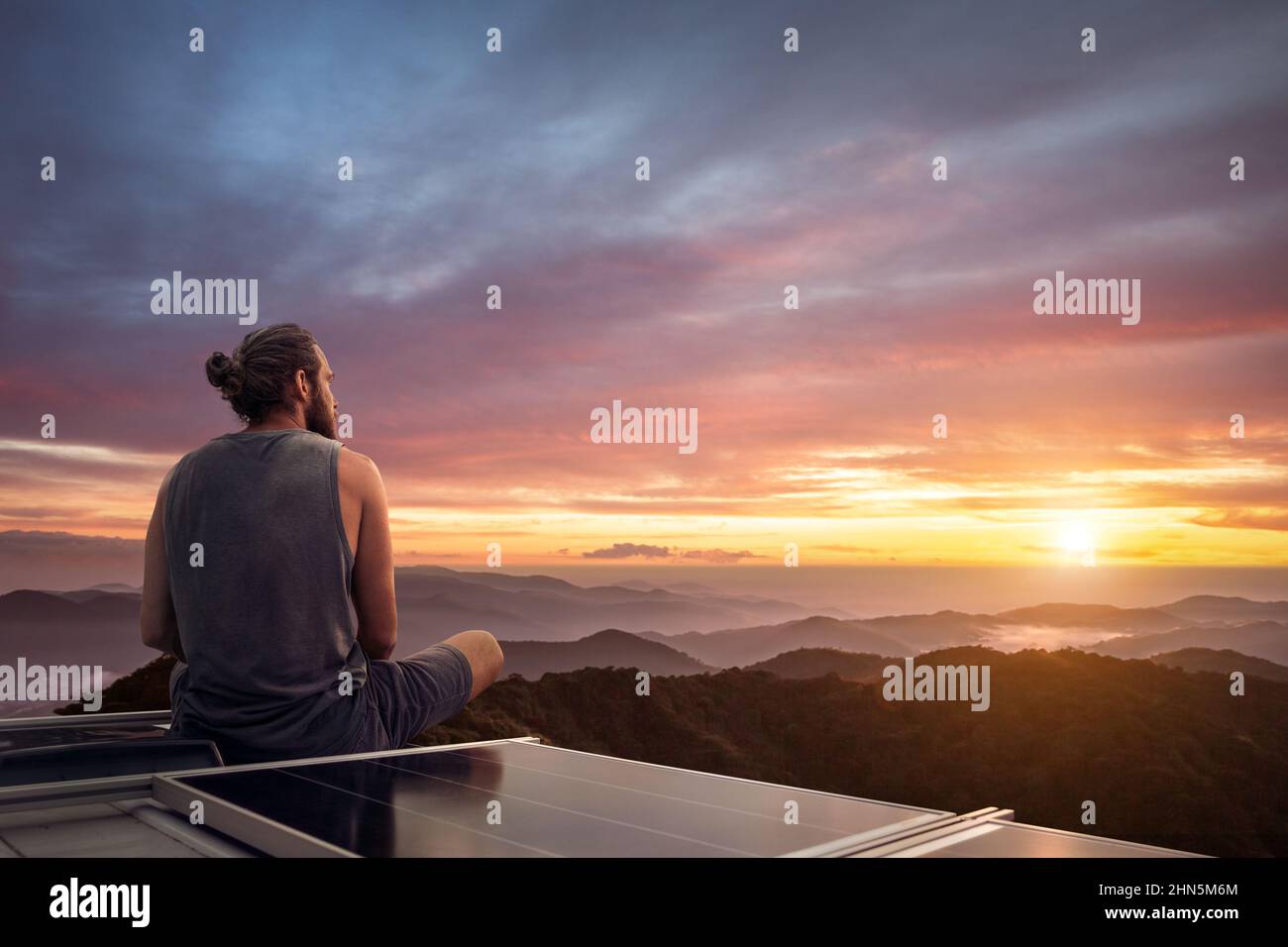 Uomo che guarda un bellissimo tramonto dal tetto di un camper Foto Stock