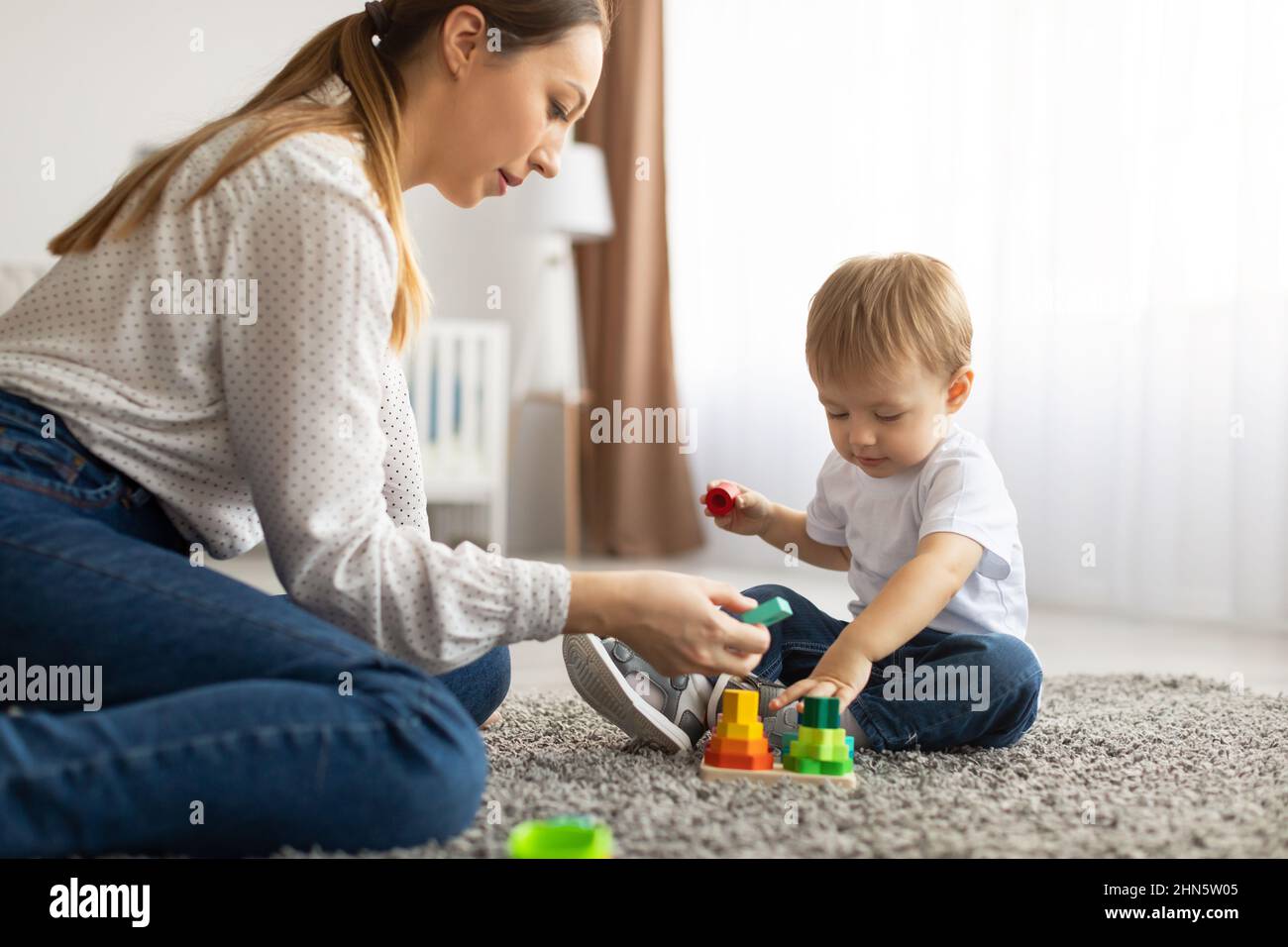 Mamma e bambino giocano insieme a casa, utilizzando i giocattoli mentre si siedono sul tappeto del pavimento in soggiorno Foto Stock