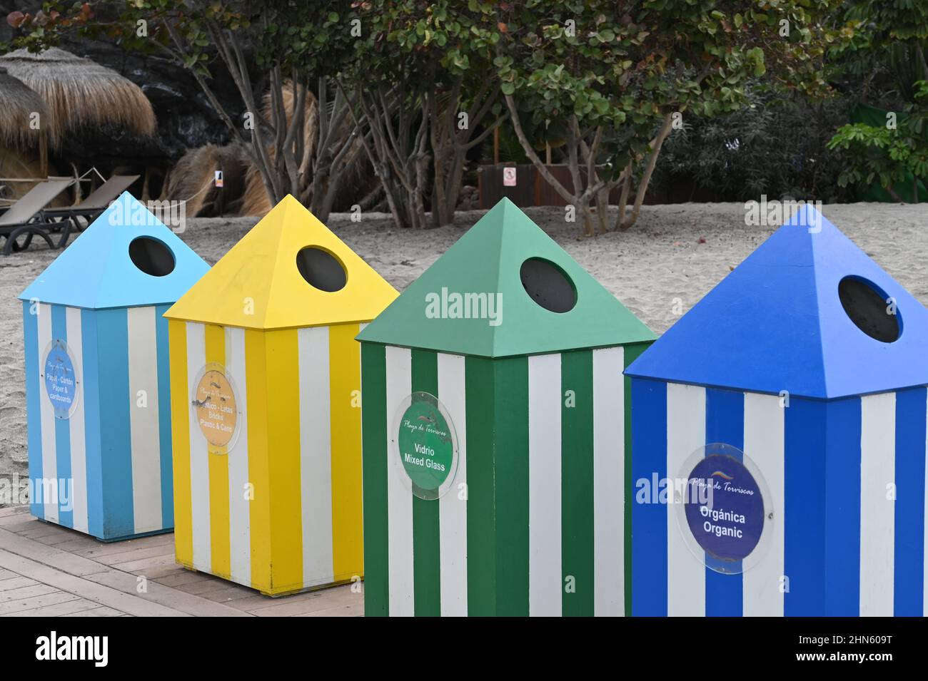 Una serie di bidoni di riciclaggio su una spiaggia a Costa Adeje, Tenerife, che assomigliano a tende nelle tonalità del blu, giallo e verde Foto Stock