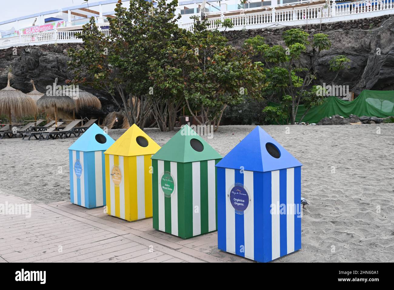 Una serie di bidoni di riciclaggio su una spiaggia a Costa Adeje, Tenerife, che assomigliano a tende nelle tonalità del blu, giallo e verde Foto Stock