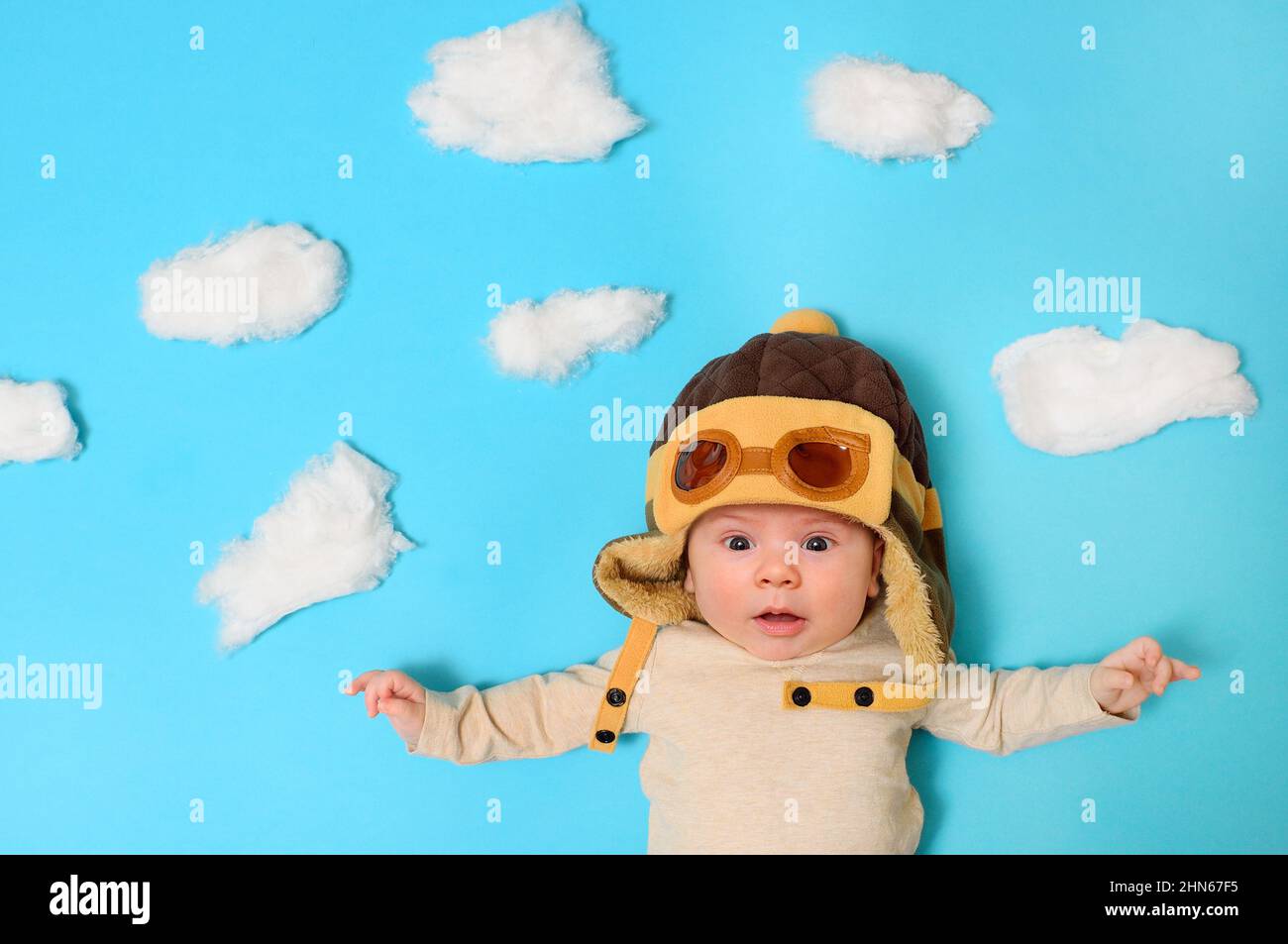 bambino in casco di un pilota contro un cielo artificiale e le nuvole di lana di cotone. Foto Stock