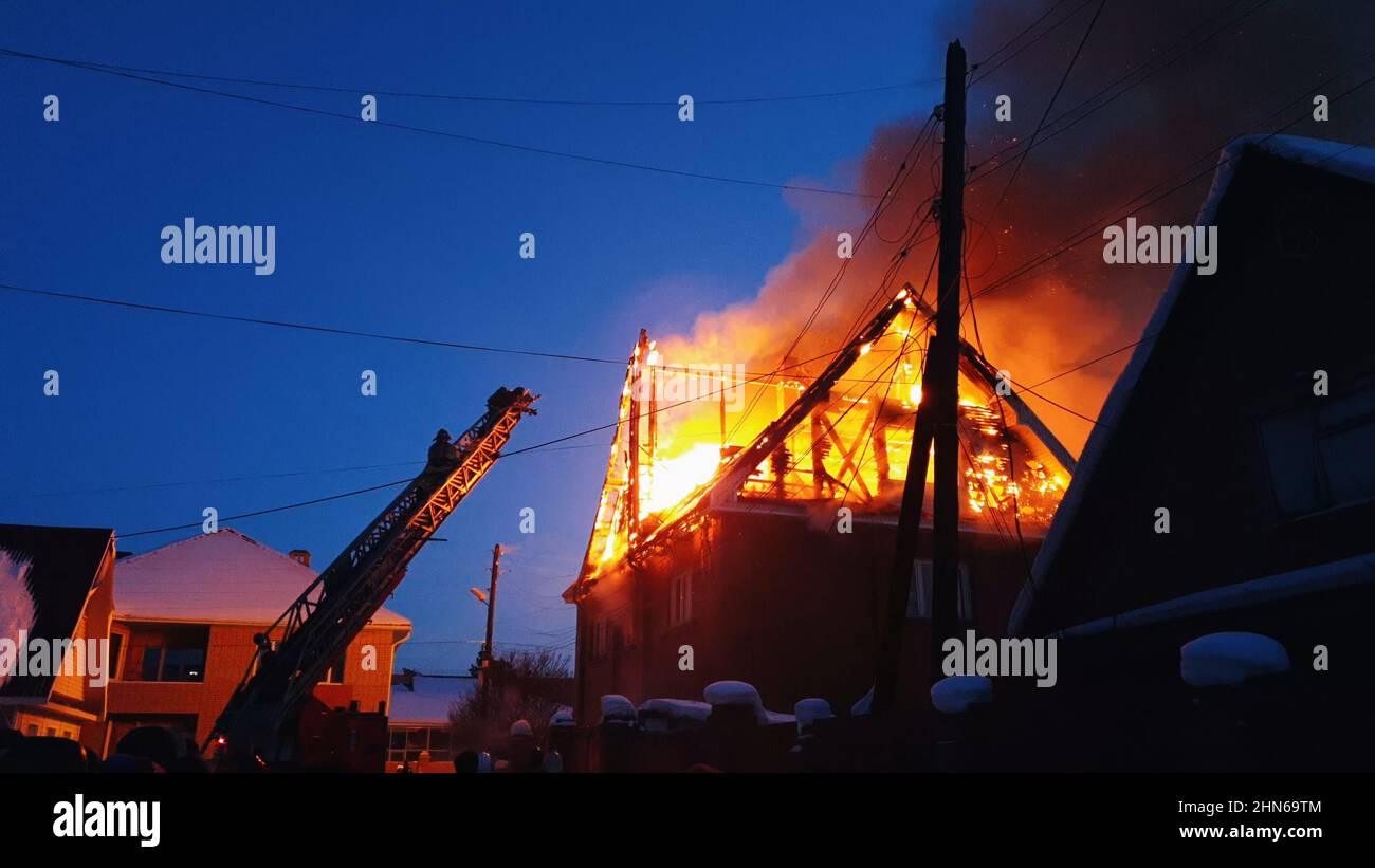 Il tetto della casa è sul fuoco. L'edificio residenziale bruciare, villaggio. I vigili del fuoco sparano dalla gru dall'alto. Il Dipartimento dei vigili del fuoco che mette fuori la fiamma libera. Fumo e scintille. Foto Stock