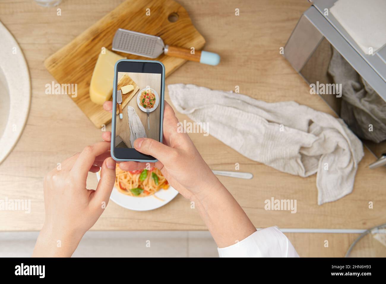 Vista dall'alto di una donna irriconoscibile con smartphone scattando foto di piatto con pasta con salsa di pomodoro per blog culinario a casa. registratore per alimenti Foto Stock