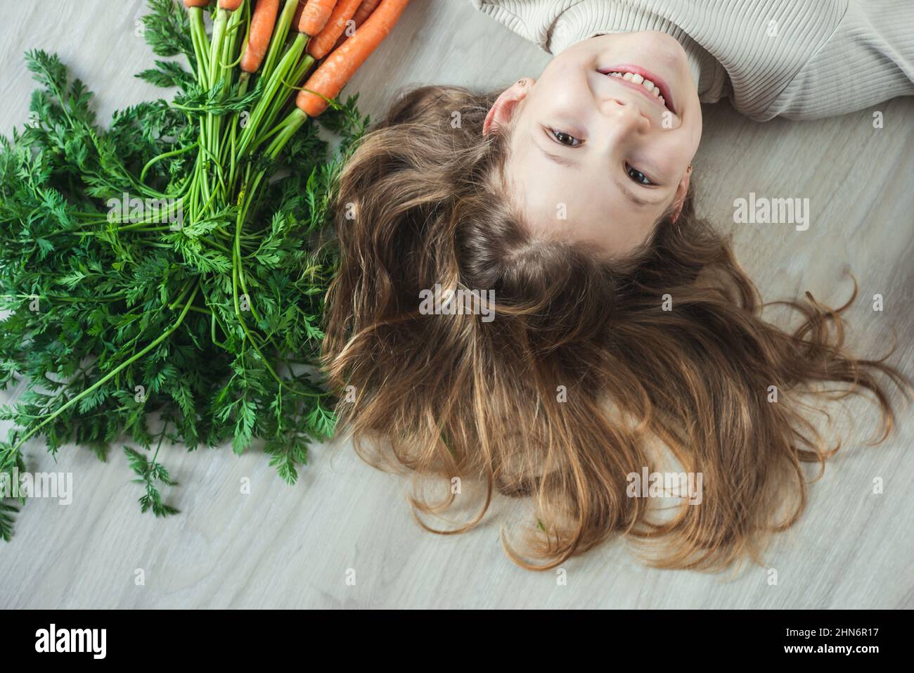 Sorridente ragazza felice teen sdraiata sul pavimento con un mazzo di carote fresche di arancio Foto Stock