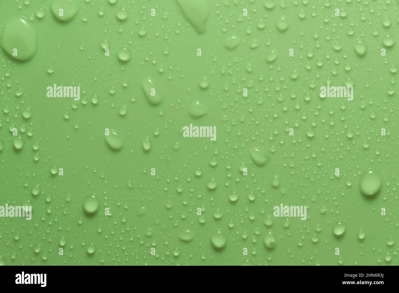 Gocce d'acqua color pastello verde su una superficie chiara e lucida Foto Stock