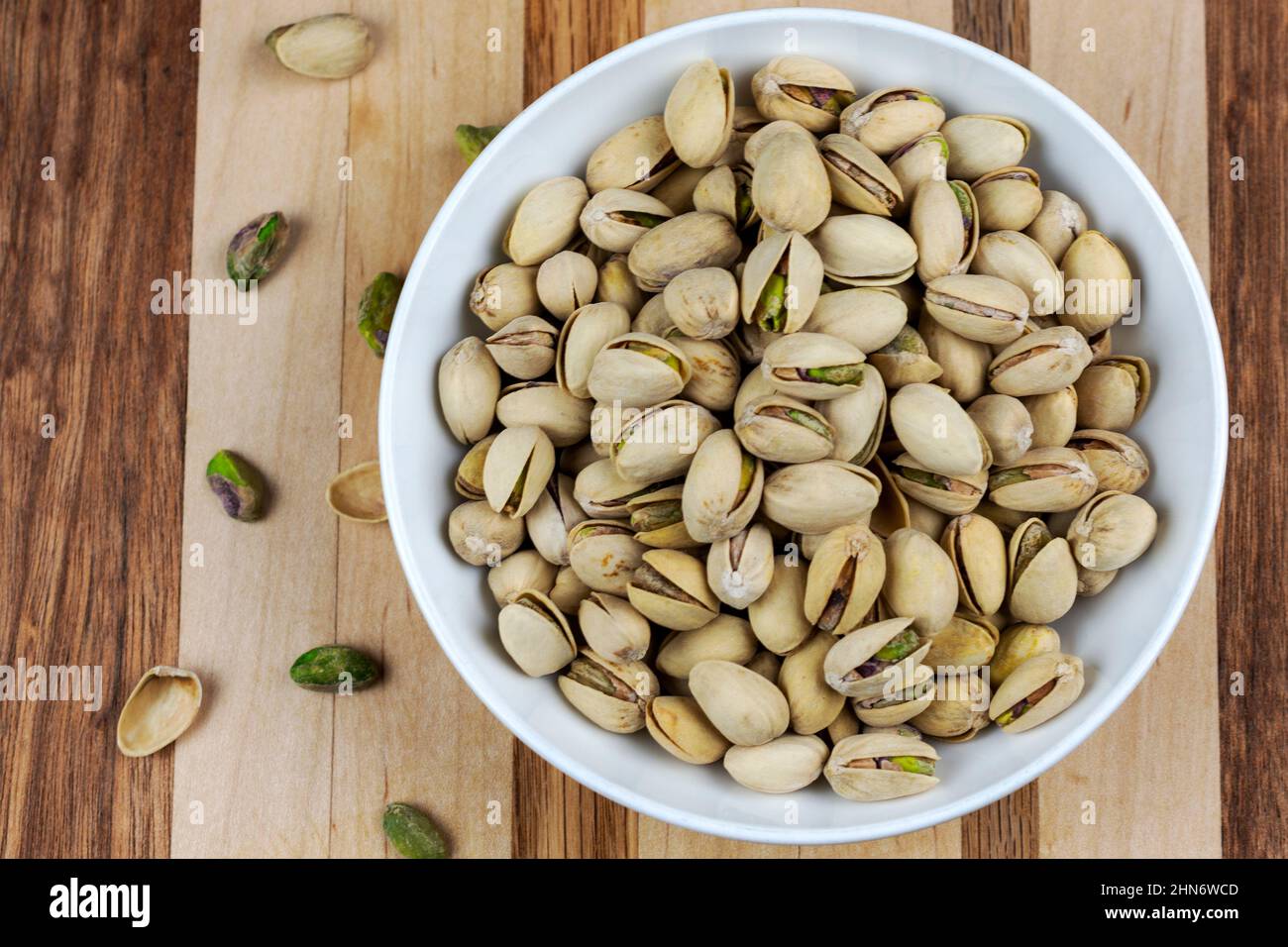Una ciotola bianca è riempita di pistacchi. Pistacchi aggiuntivi crattered a sinistra. Macellaio blocco legno sfondo. Foto Stock