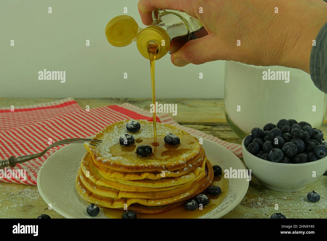 Primo piano di versare lo sciroppo d'acero su una pila di pancake. Impila di pancake con mirtilli freschi versati con sciroppo d'acero Foto Stock