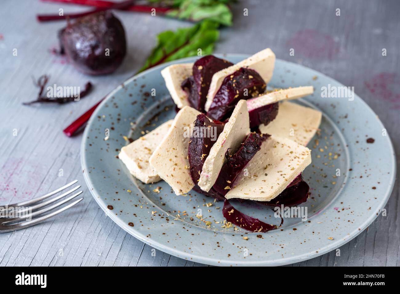 Tofu a fette con barbabietola rossa al forno su piatto, forchetta e foglia verde sul tavolo. Foto Stock