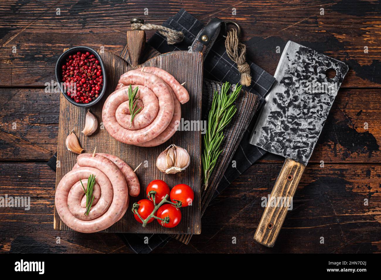 Salsicce bavaresi crudi a spirale su un asse di legno. Sfondo in legno. Vista dall'alto. Foto Stock