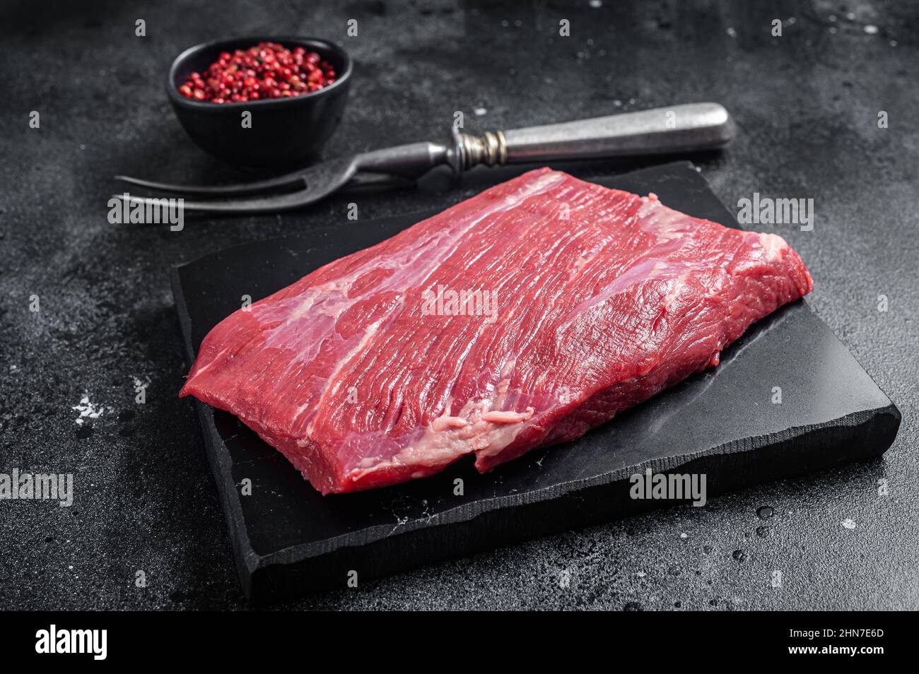 Bistecca di prima scelta sul fianco, carne di manzo cruda su tavola di marmo con erbe aromatiche. Sfondo nero. Vista dall'alto Foto Stock
