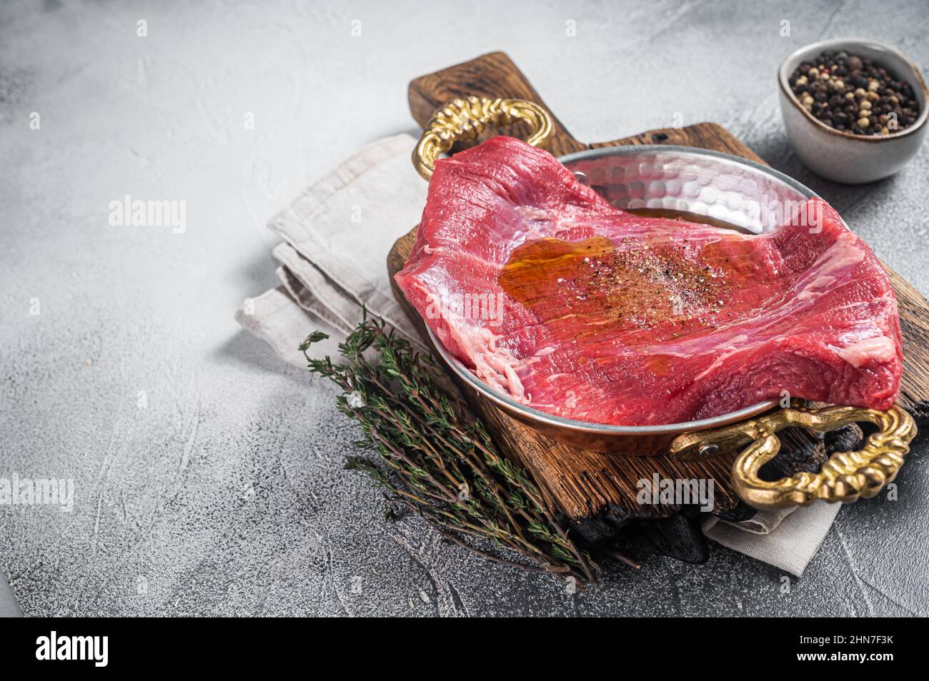Bistecca con patta o fianco, carne di manzo cruda in padella con erbe e olio d'oliva. Sfondo bianco. Vista dall'alto. Spazio di copia Foto Stock