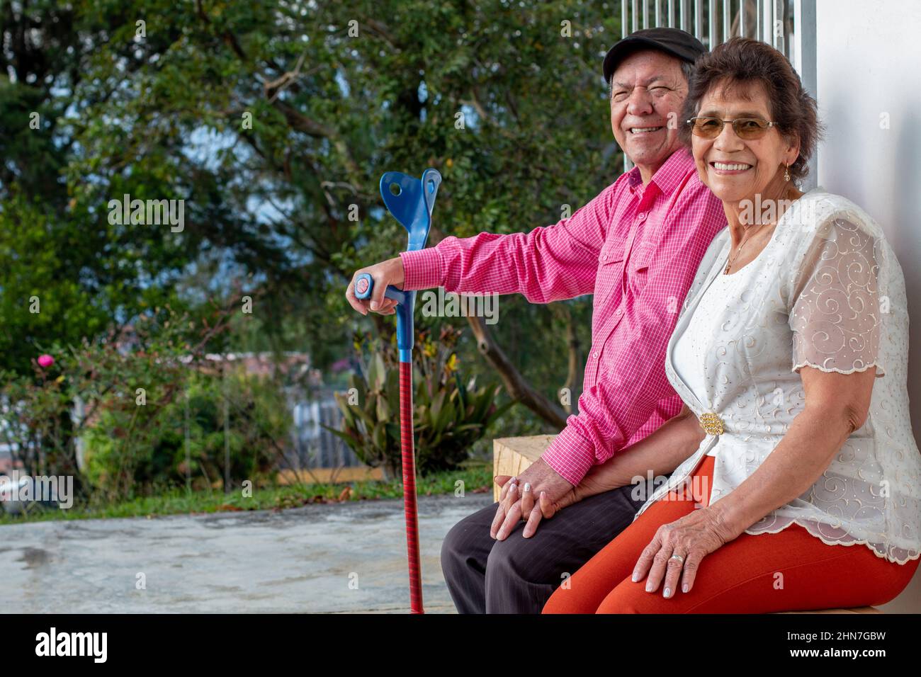 Coppia sposata anziana che guarda la macchina fotografica mentre sorride. Coppia anziana seduta su una panca di legno nel cortile della loro fattoria in natura. Foto Stock