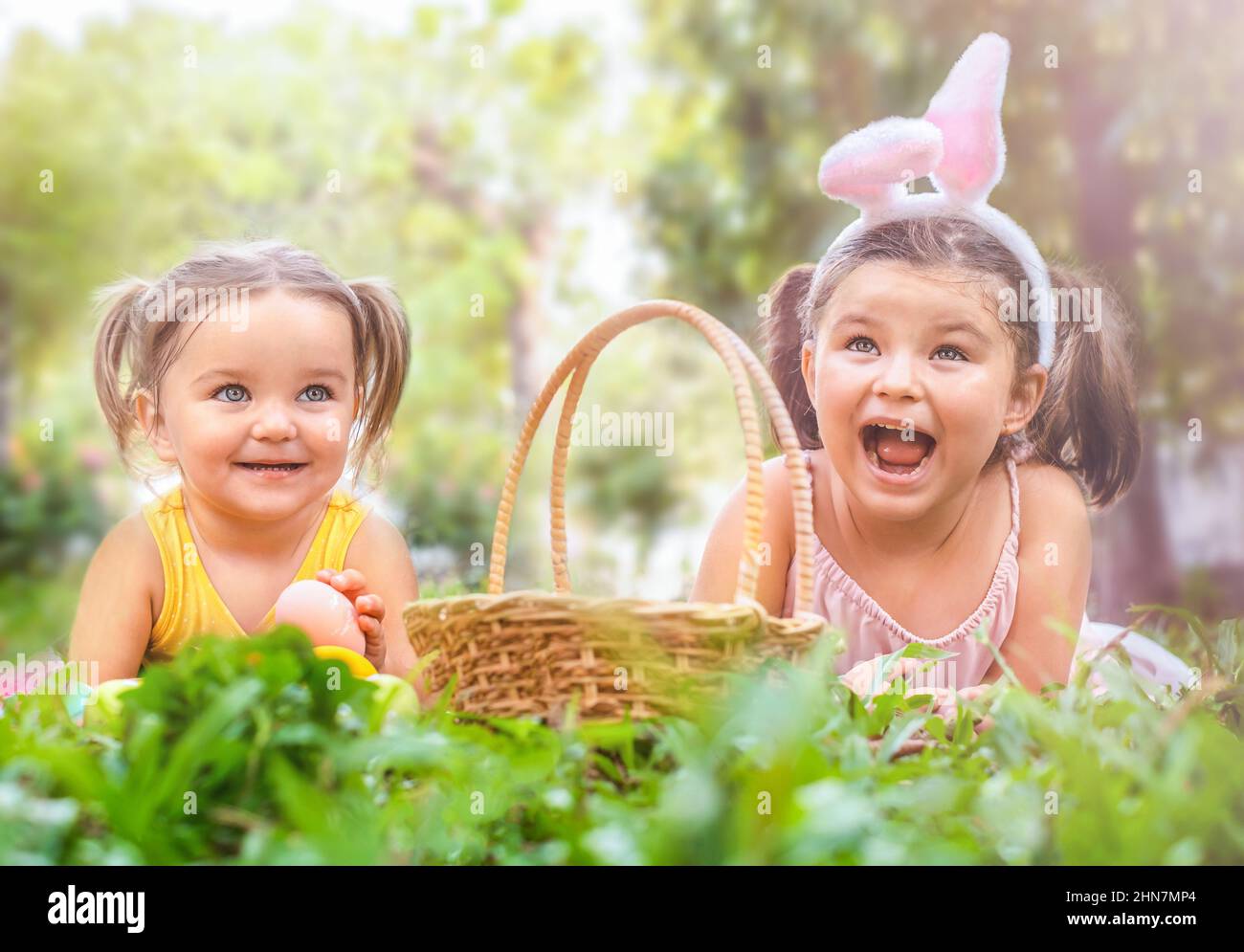 I bambini della sorella si trovano sull'erba con un cestino e le uova di Pasqua nel cortile Foto Stock