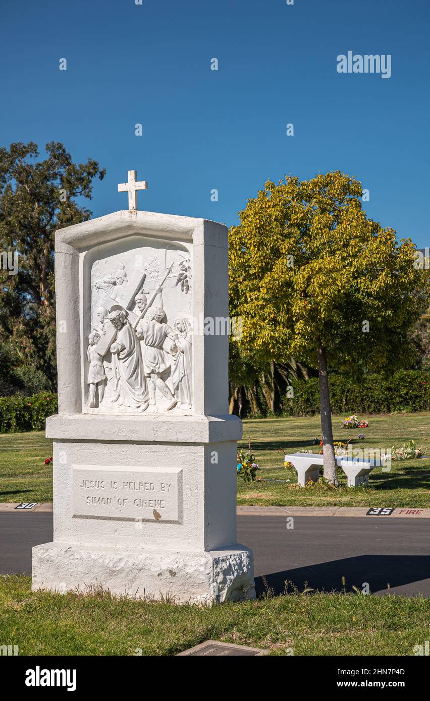 Santa Barbara, California, USA - 8 febbraio 2022: Cimitero di Calvario. Primo piano, statua bianca della Stazione della Croce 5 sul prato verde sepoltura sotto il blu s. Foto Stock