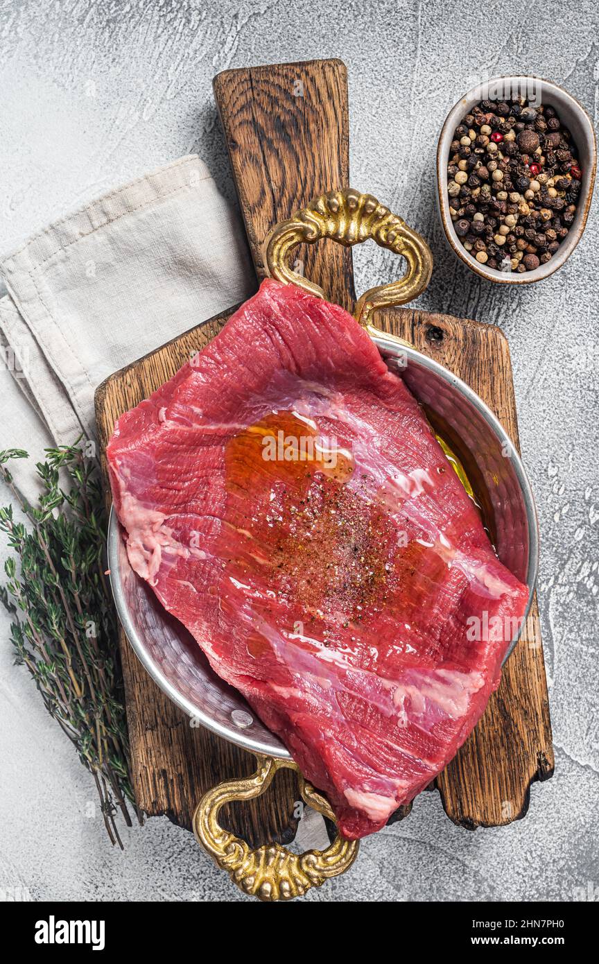 Bistecca con patta o fianco, carne di manzo cruda in padella con erbe e olio d'oliva. Sfondo bianco. Vista dall'alto Foto Stock