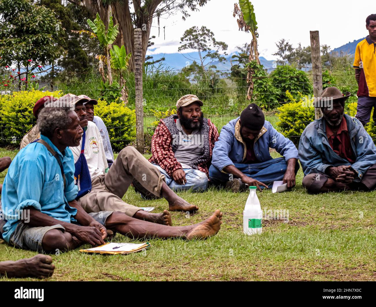 Gli anziani del Papuan seduti sull'erba durante un incontro di comunità, ascoltando attentamente l'oratore Foto Stock