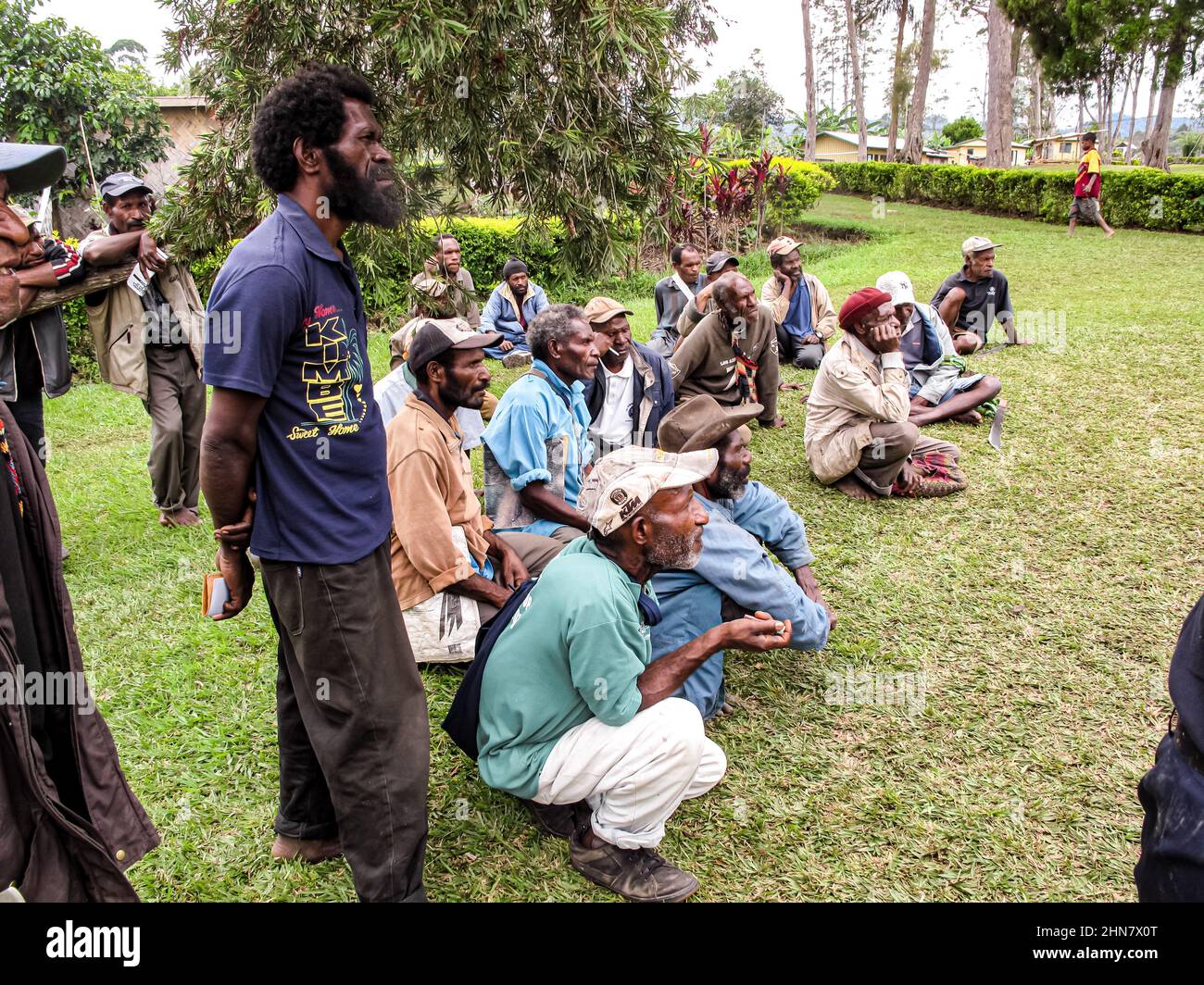 Gli anziani del Papuan seduti sull'erba durante un incontro di comunità, ascoltando attentamente l'oratore Foto Stock