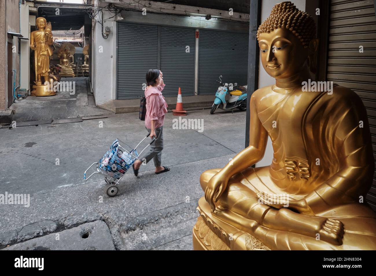 Una donna passa statue di Buddha poste fuori dai negozi di oggetti buddisti; Bambung Muang Rd., Bangkok, Thailandia Foto Stock