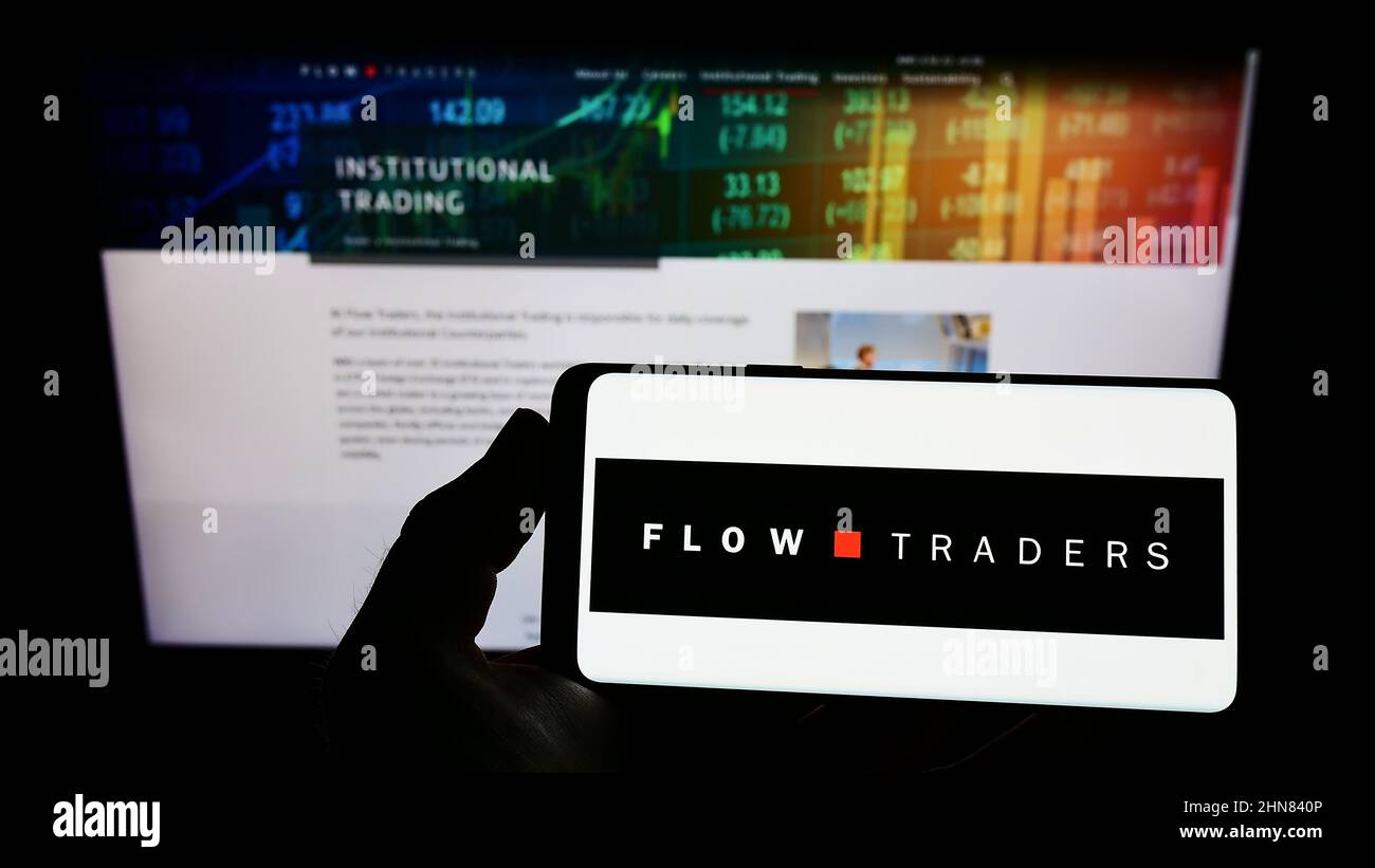Persona che tiene smartphone con il logo della società finanziaria olandese Flow Traders N.V. sullo schermo di fronte al sito web. Mettere a fuoco sul display del telefono. Foto Stock