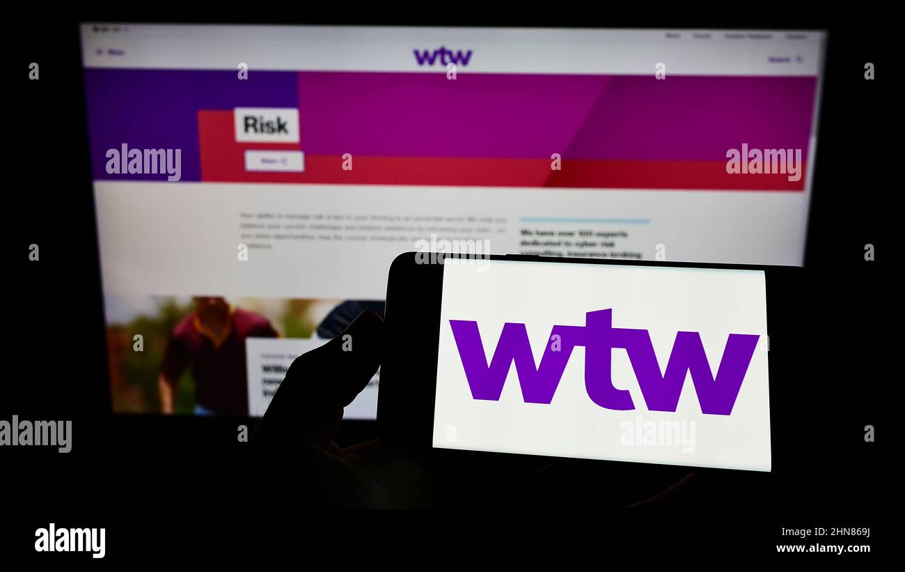 Persona che tiene il cellulare con il logo della società finanziaria Willis Towers Watson plc (WTW) sullo schermo di fronte al sito web. Mettere a fuoco sul display del telefono. Foto Stock