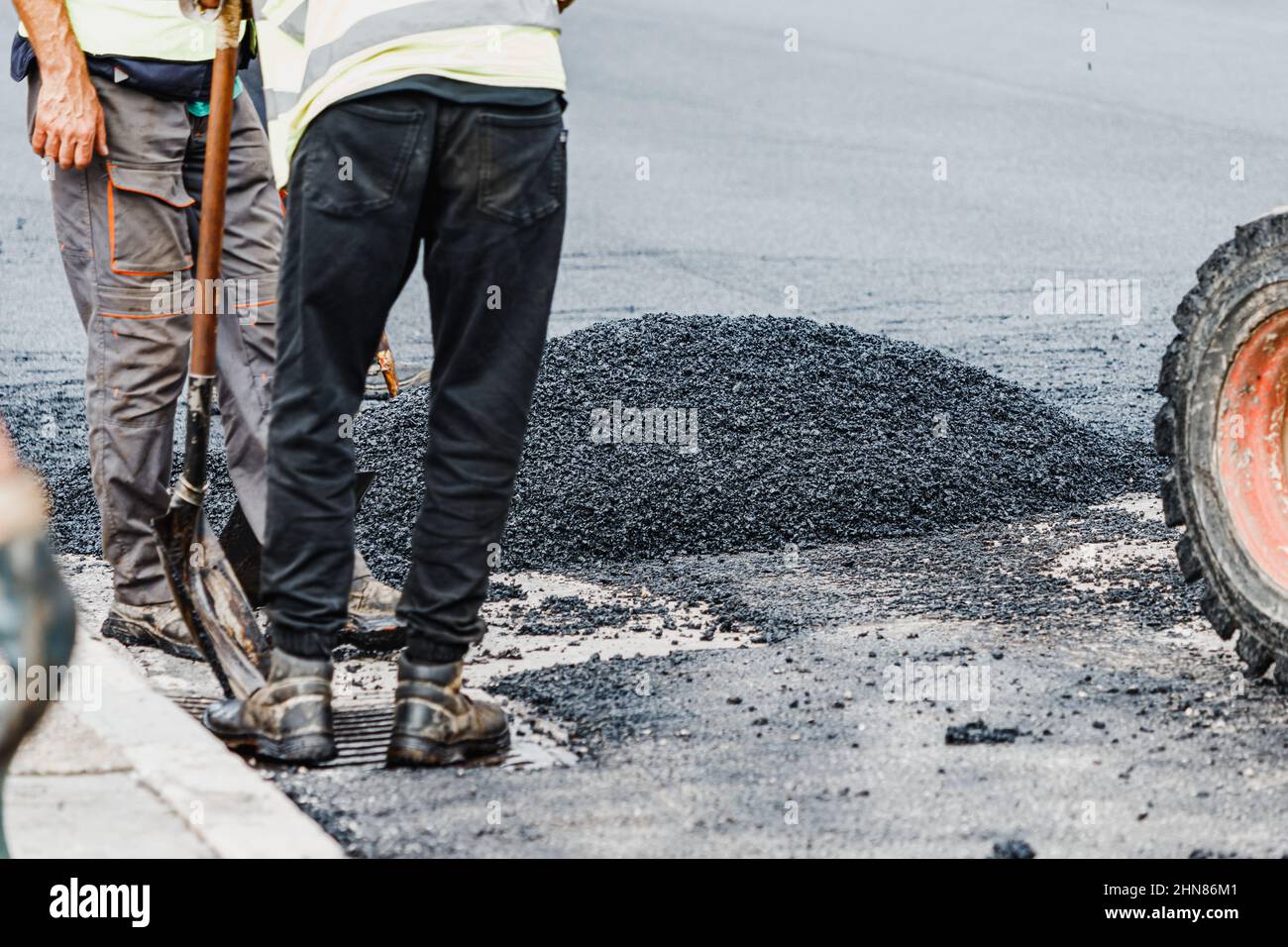 Lavori manuali pesanti e sporchi sulla posa di asfalto e bitume freschi su una strada cittadina Foto Stock