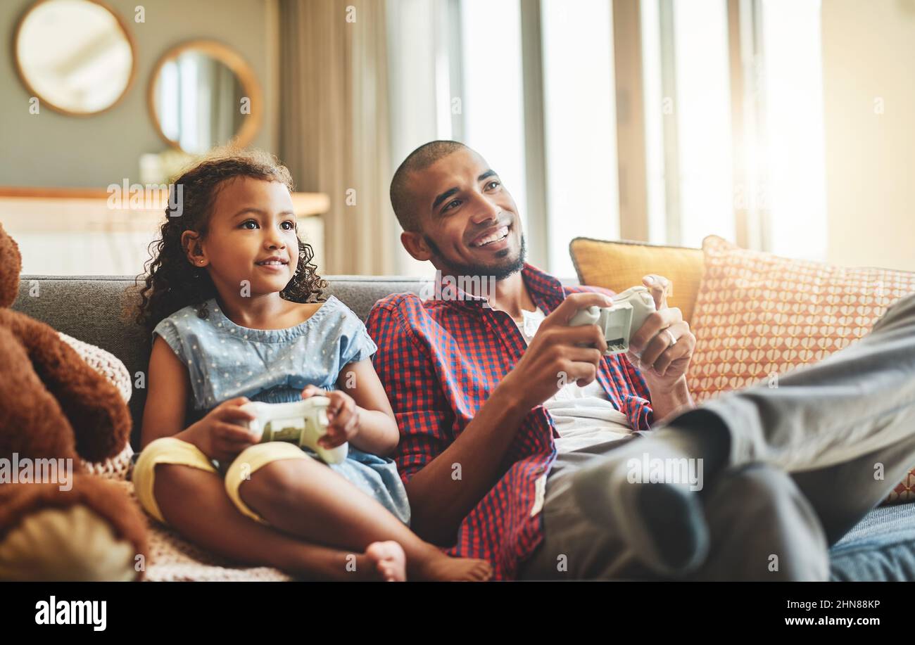 Anni dopo diventerebbe una videogamer professionista. Scatto di una bambina adorabile e suo padre che giocano i videogiochi insieme sul divano a casa. Foto Stock