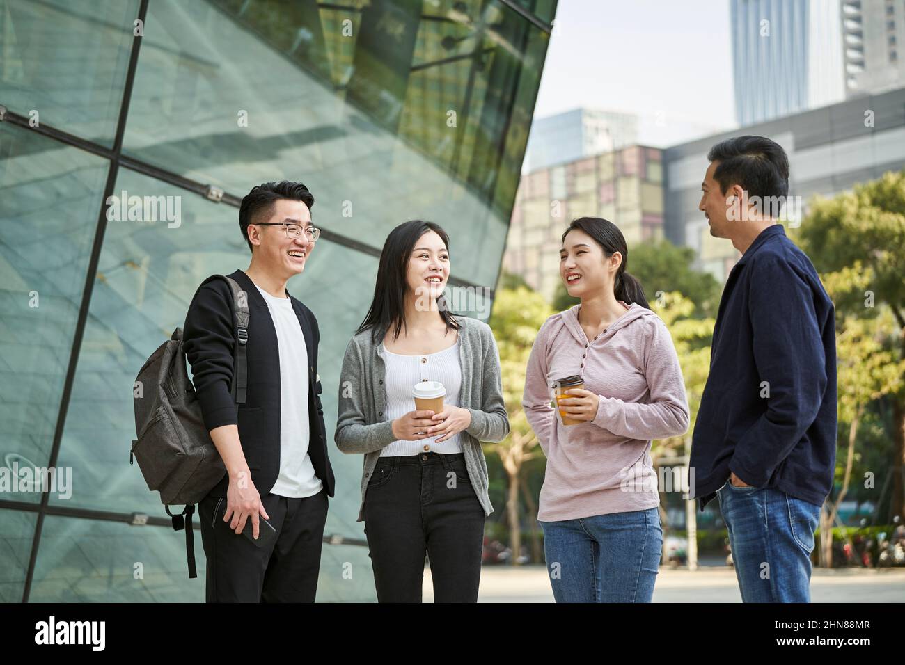 giovani asiatici in piedi parlando per strada felice e sorridente Foto Stock