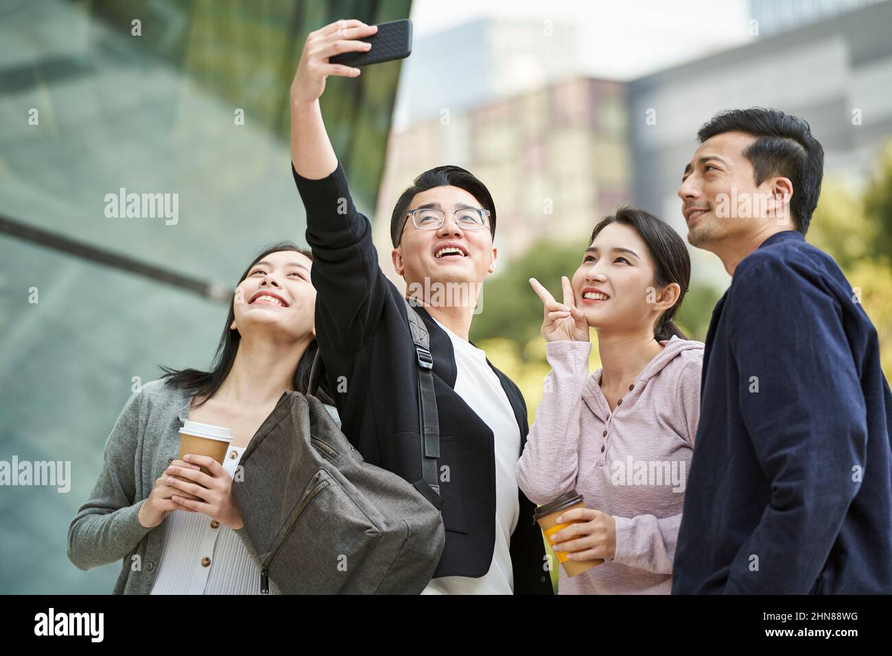 gruppo di giovani asiatici che prendono un selfie utilizzando il cellulare all'aperto sulla strada felice e sorridente Foto Stock